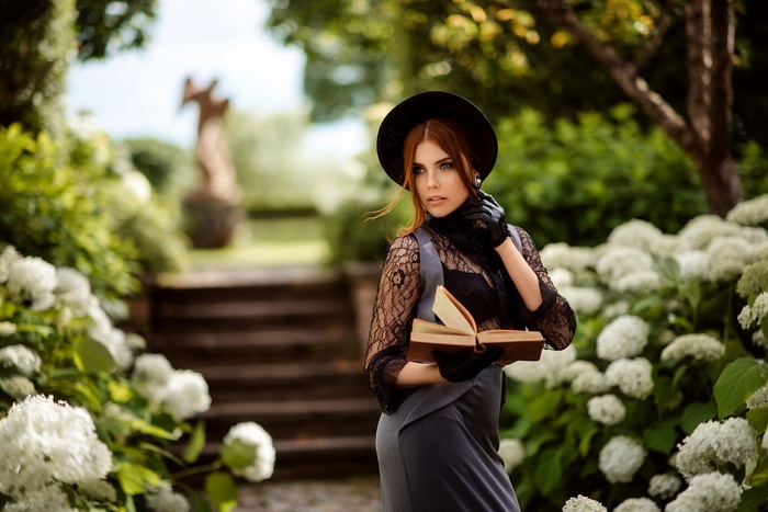 Woman in black hat and gloves holding a book in a garden