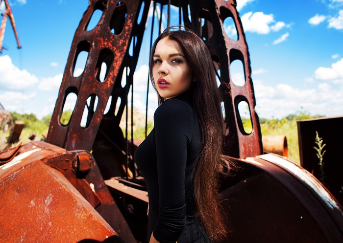 Woman in black clothing with long hair near rusty machinery