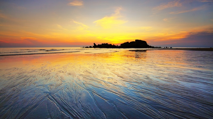 Sunset over a beach with rock formations and waves