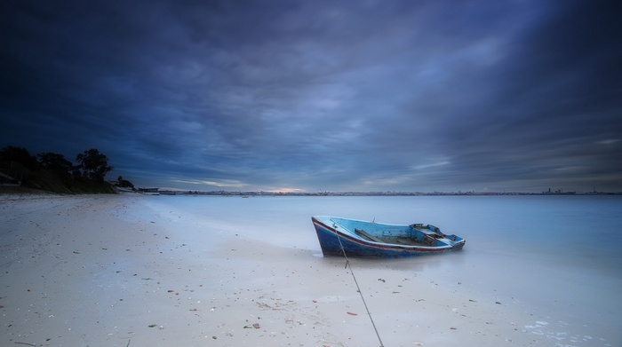 Abandoned blue boat on a sandy beach at dusk