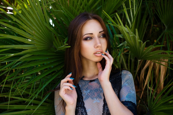 Woman with painted nails in front of palm leaves