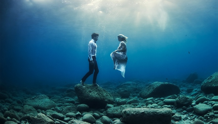 Couple underwater among rocks and fish