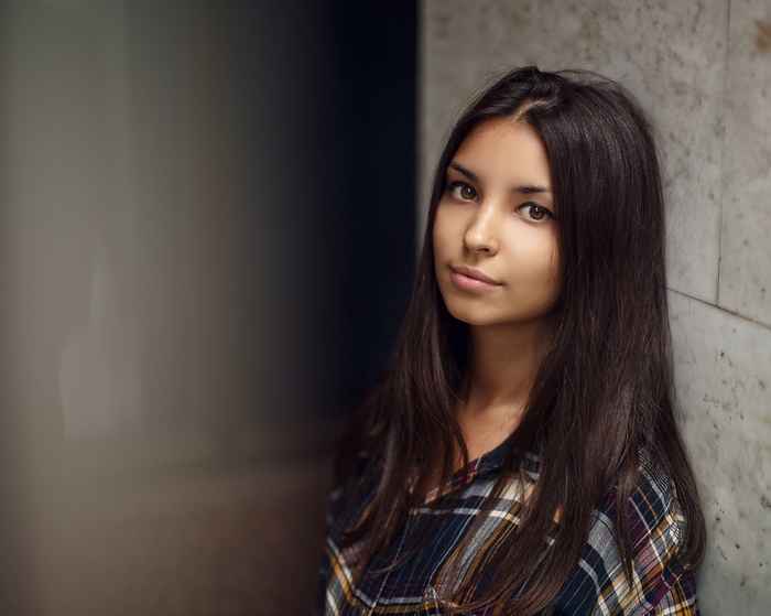 Young woman in plaid shirt leaning against wall