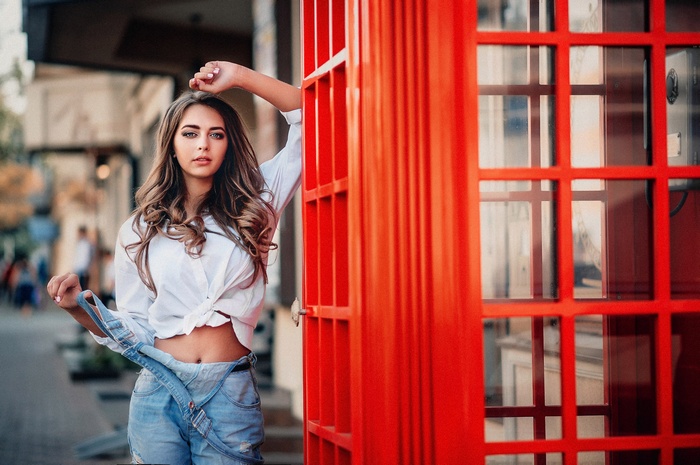 Woman in overalls and white shirt by red phone booth