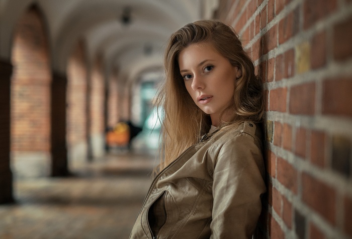 Woman in leather jacket leaning against brick wall