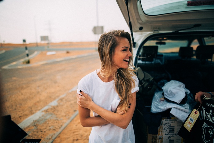 Woman with blonde hair laughing by a car