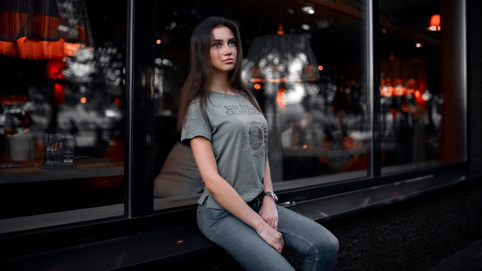 Woman in T-shirt and jeans sitting by a window