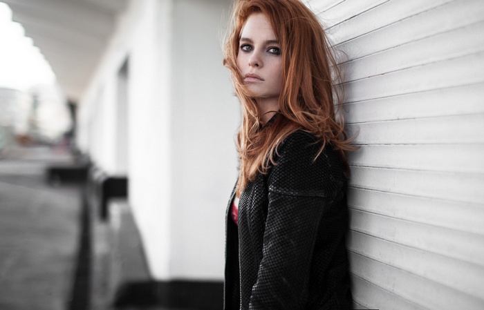 Redhead woman in leather jacket leaning against a wall