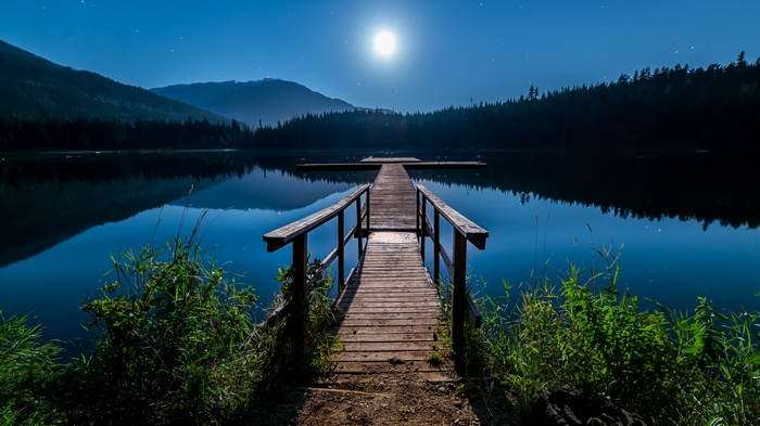 Moonlit lake with a wooden dock and mountains