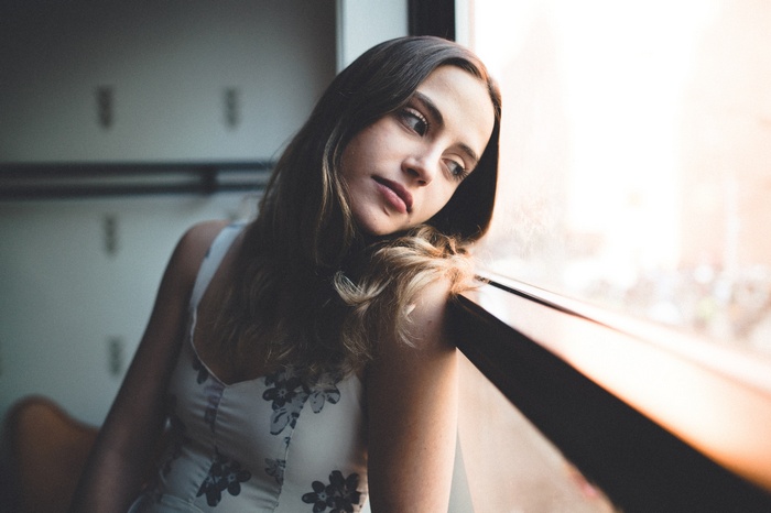Woman in white floral dress looking out a window