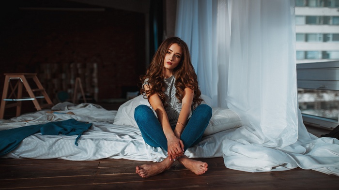 Woman with long brown hair sitting on a bed