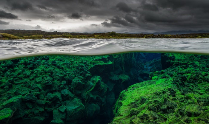 Underwater rock formations with green algae and stormy sky