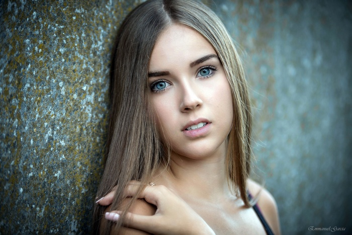 Portrait of a young woman with blue eyes leaning against a wall