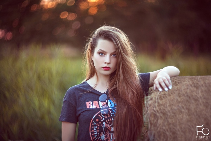 Woman with long brown hair and red lipstick leaning on hay bale