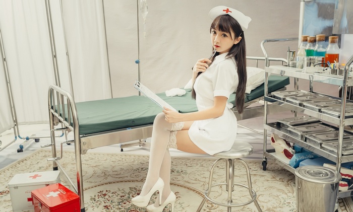 Asian nurse in outfit sitting on stool with clipboard