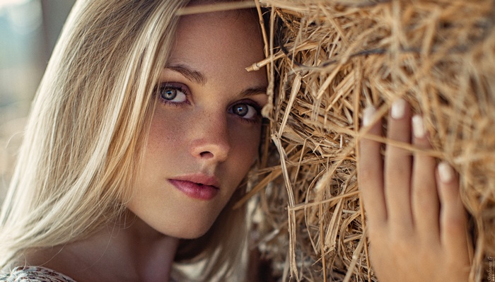 Woman with blonde hair and blue eyes near hay