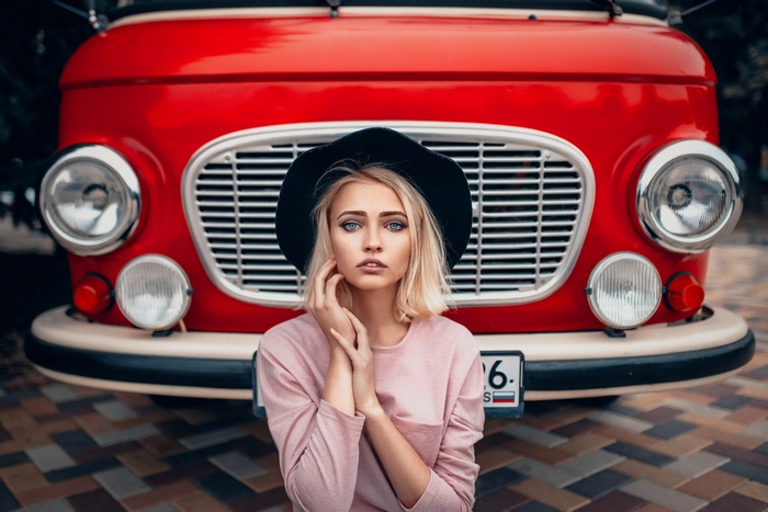 Woman with blonde hair and blue eyes wearing a hat in front of a red Barkas