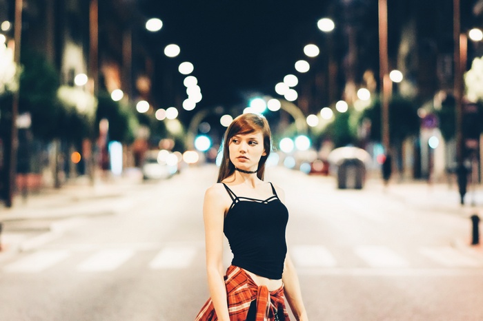 Woman in black top and plaid shirt on a street at night