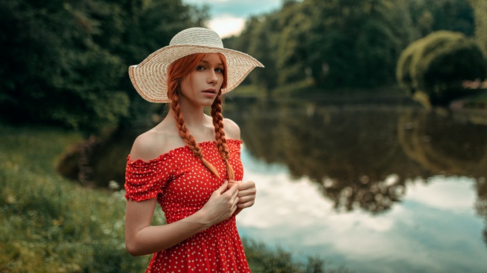 Woman with red braids and hat by a lake