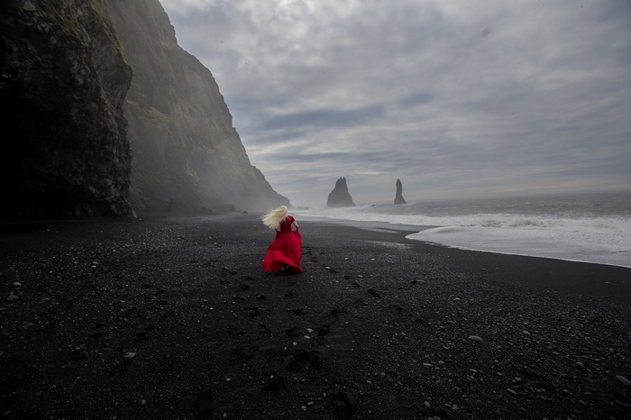 Woman in red dress on black sand beach with sea stacks