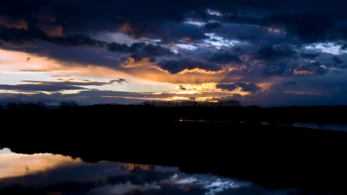 Sunset over a dark landscape with water reflection