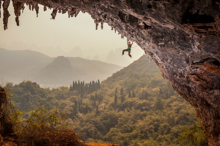 Rock climber hanging from cave overhang with karst mountains in background