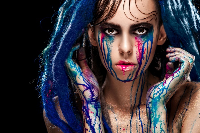 Woman with blue hair and colorful paint on face and hands