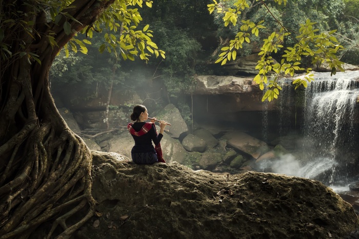Woman playing flute by waterfall in nature