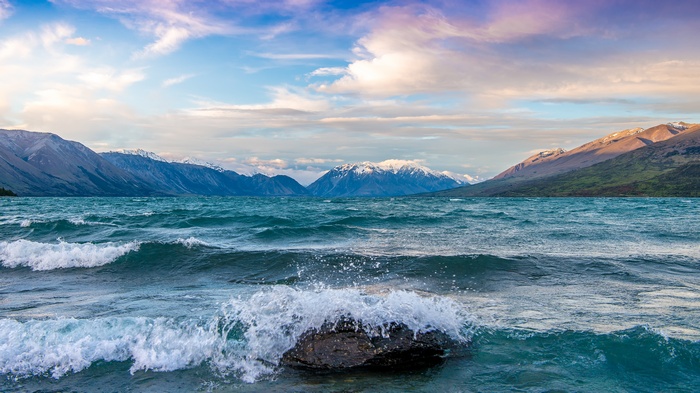 Waves crashing on a rock in a lake with mountains