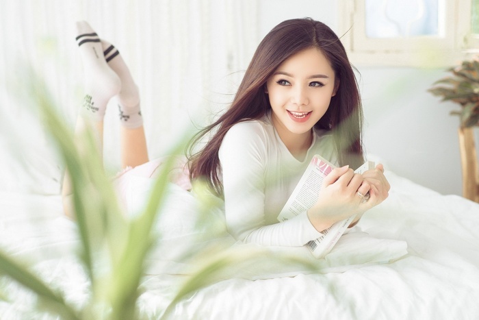 Asian woman lying on bed reading a book