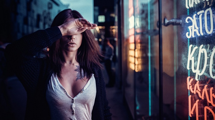 Woman with hand over face near neon sign