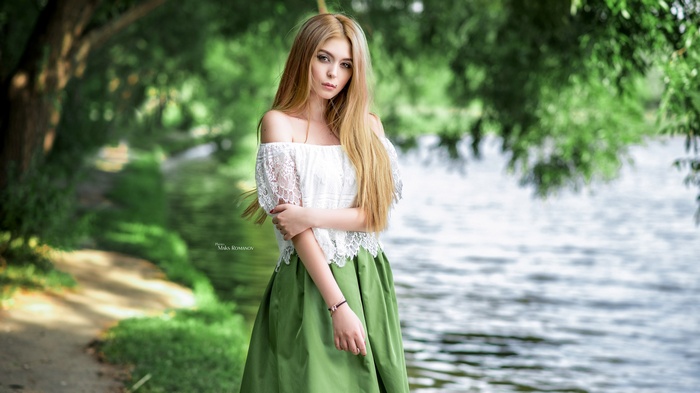 Woman with blonde hair in a white top and green skirt by the water