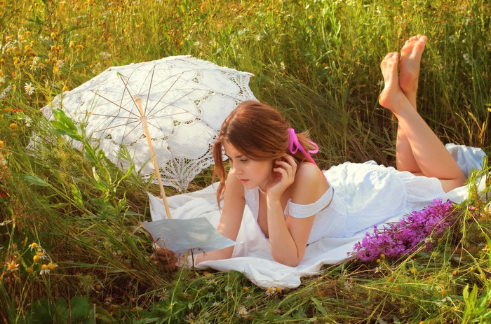 Woman reading in a field with an umbrella