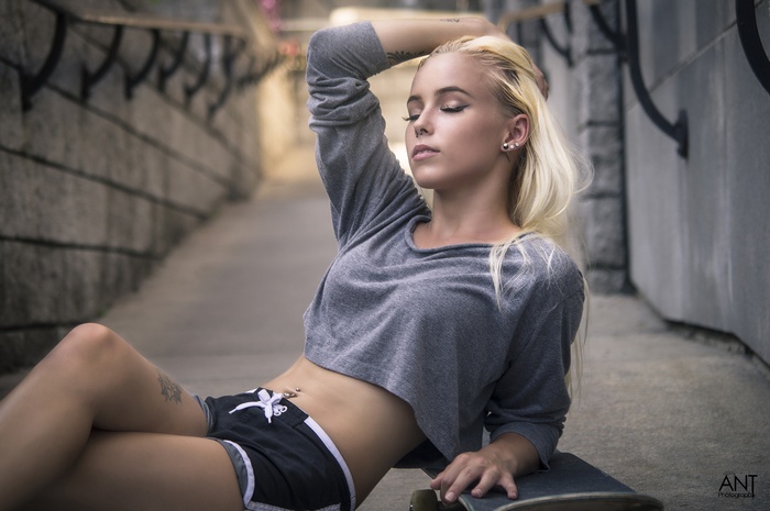 Woman with blonde hair and tattoos sitting on a skateboard