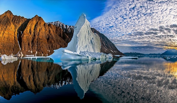 Iceberg and mountains reflected in water under cloudy sky