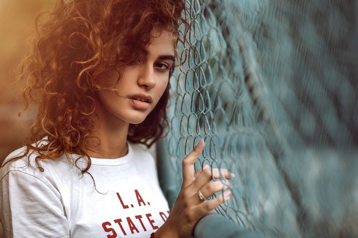 Woman with curly hair leaning on a fence