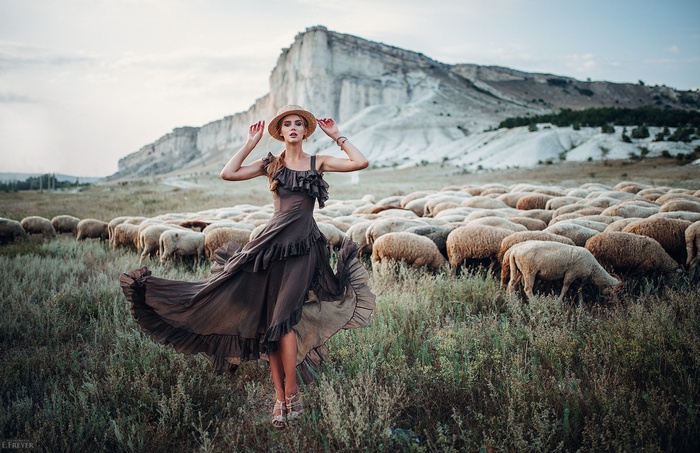 Woman in dress and hat with sheep and mountain