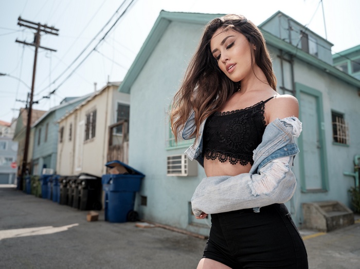 Woman in black crop top and denim jacket in alley