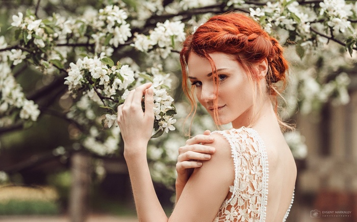 Redhead woman in white dress near blooming tree