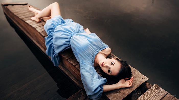 Woman in blue dress lying on a wooden pier