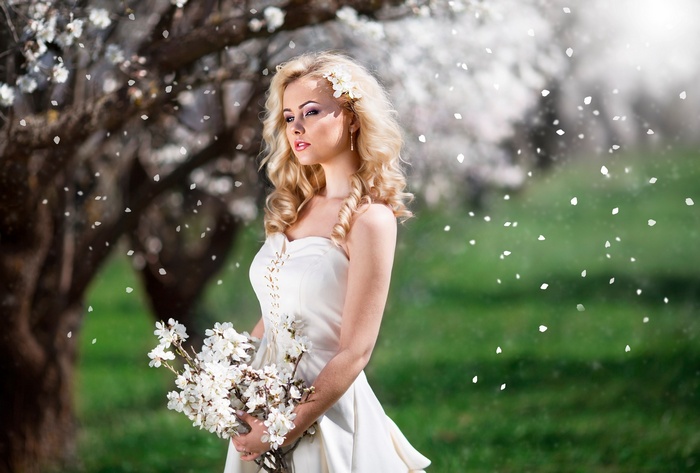 Blonde woman in white dress holding flowers outdoors