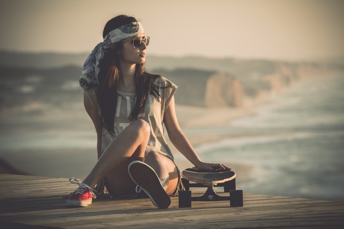 Woman with bandana and sunglasses sitting with skateboard