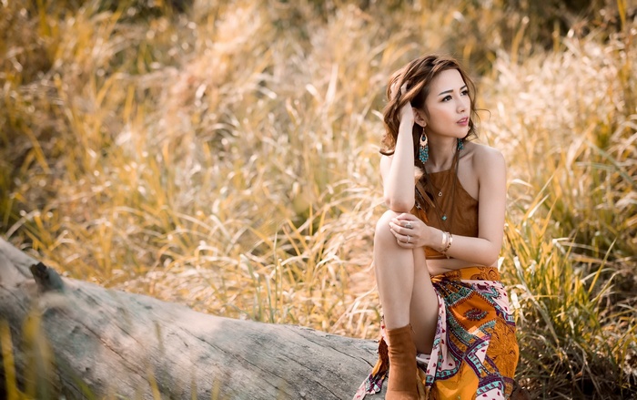Asian woman sitting on a log in a field
