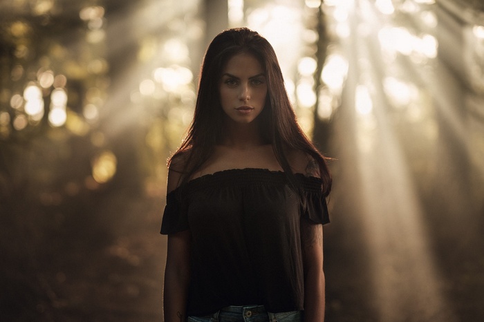 Woman with bare shoulders in a forest with sunbeams