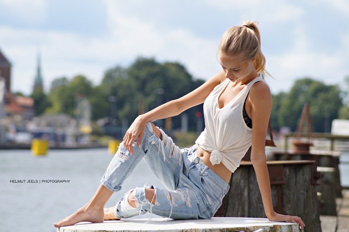 Woman with ponytail in torn jeans sitting by water