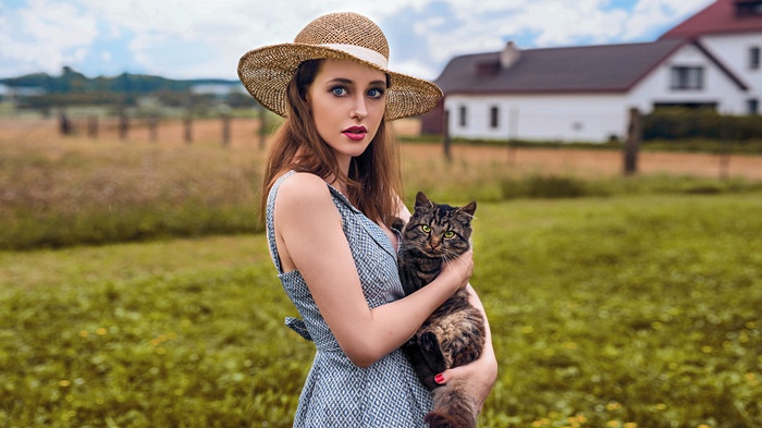 Woman in straw hat holding a cat outdoors