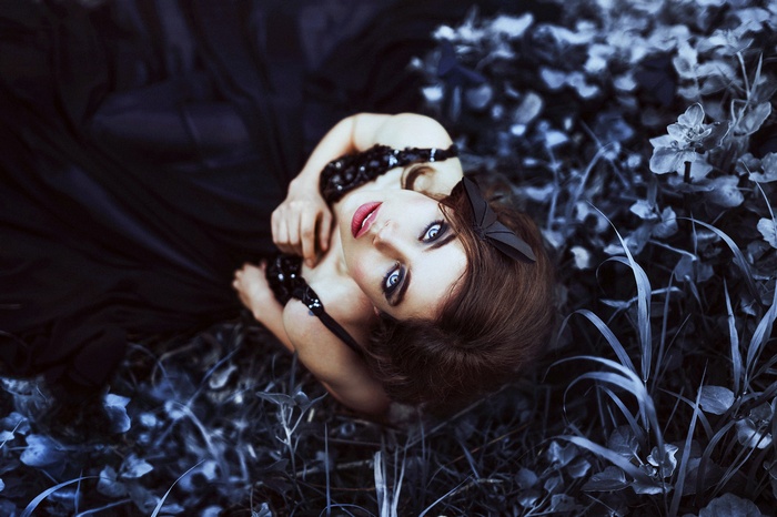 Woman with blue eyes and red lipstick in a black dress lying on leaves