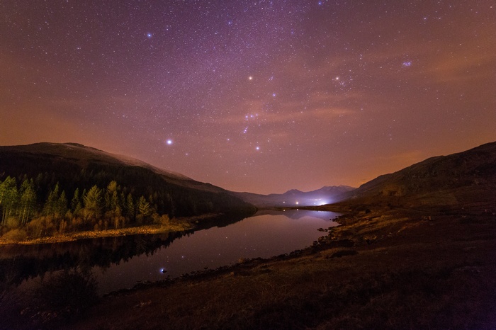 Starry night sky over a lake and forest