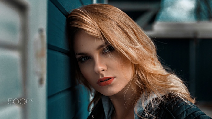 Woman with blonde hair leaning against a blue wall