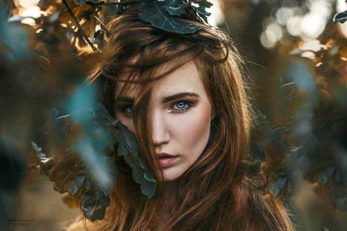 Woman with red hair and blue eyes among leaves